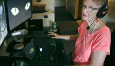 signora anziana con cuffie da gaming seduta alla scrivania con schermo computer davanti