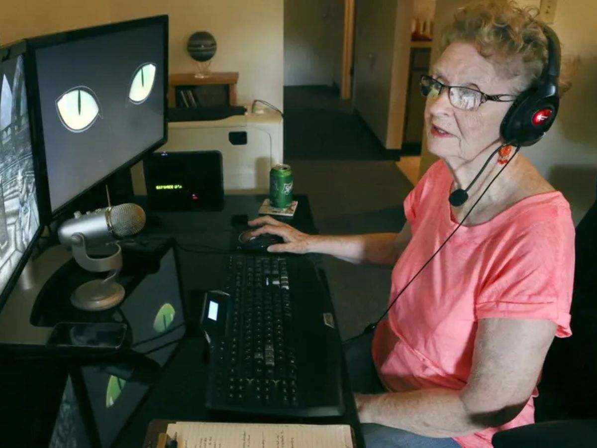 signora anziana con cuffie da gaming seduta alla scrivania con schermo computer davanti