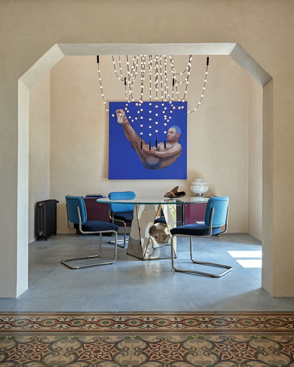 Soggiorno tavolo tondo in vetro sedie blu dipinto alla parete cementine colorate pavimento