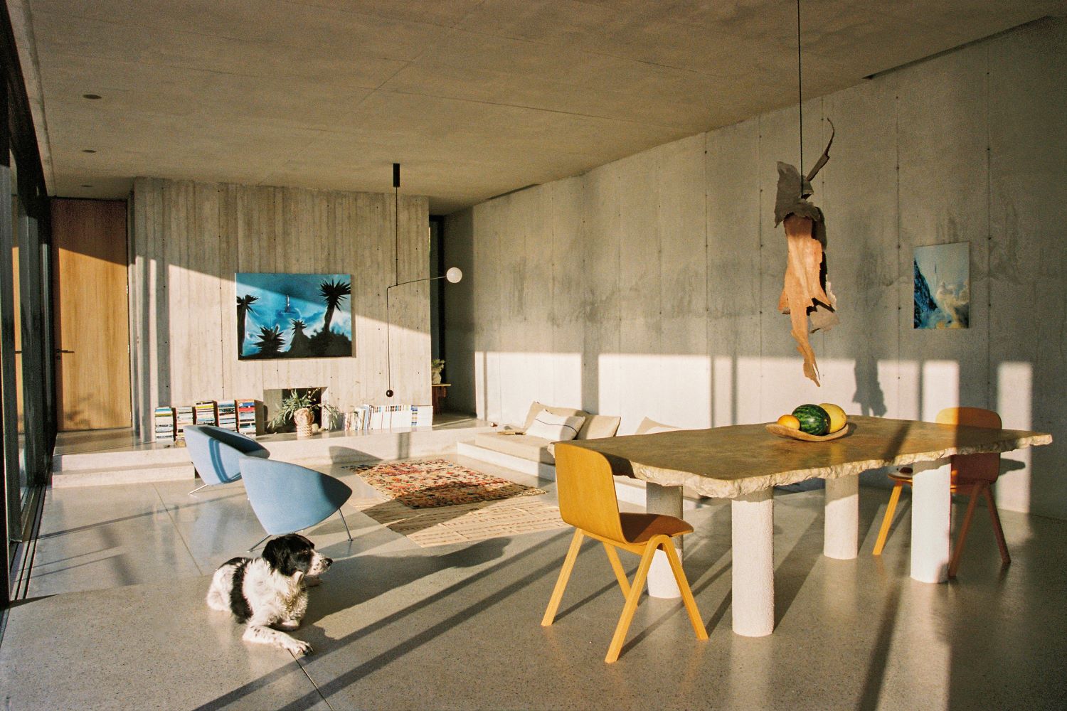 Salotto con poltrone azzurre, sedie gialle, tavolo bianco e beige e un cane