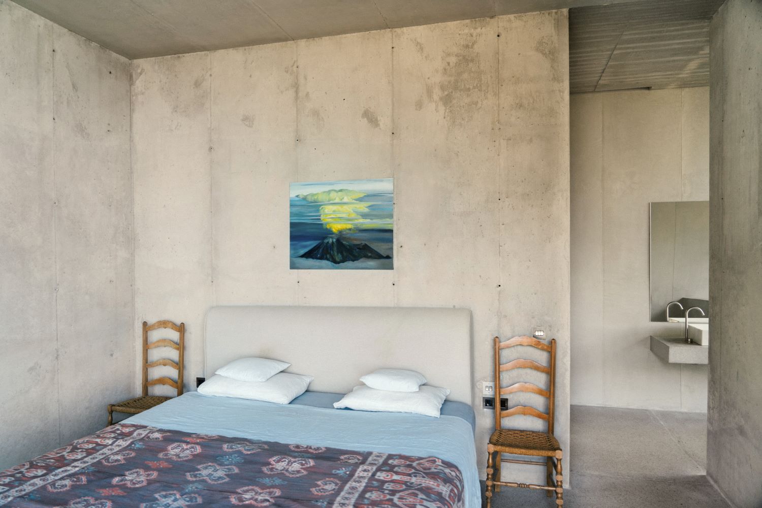 Camera da letto con letto matrimoniale, un quadro appeso alla parete e due sedie di legno ai lati del letto come comodini