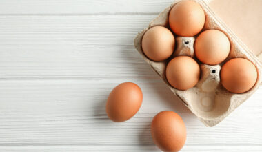 5 Uova di gallina in cartone e due uova su tavolo bianco