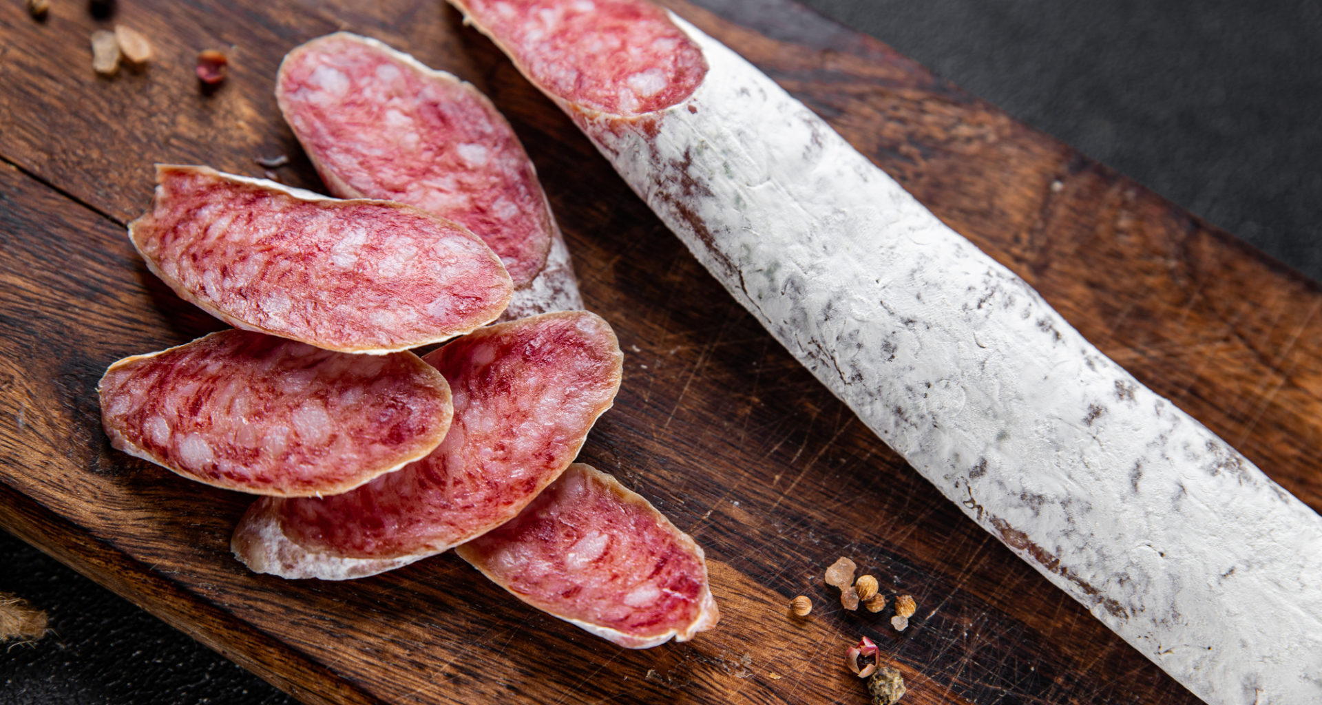 Salsiccia o salame intero e affettato su un tagliere di legno