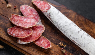 Salsiccia o salame intero e affettato su un tagliere di legno