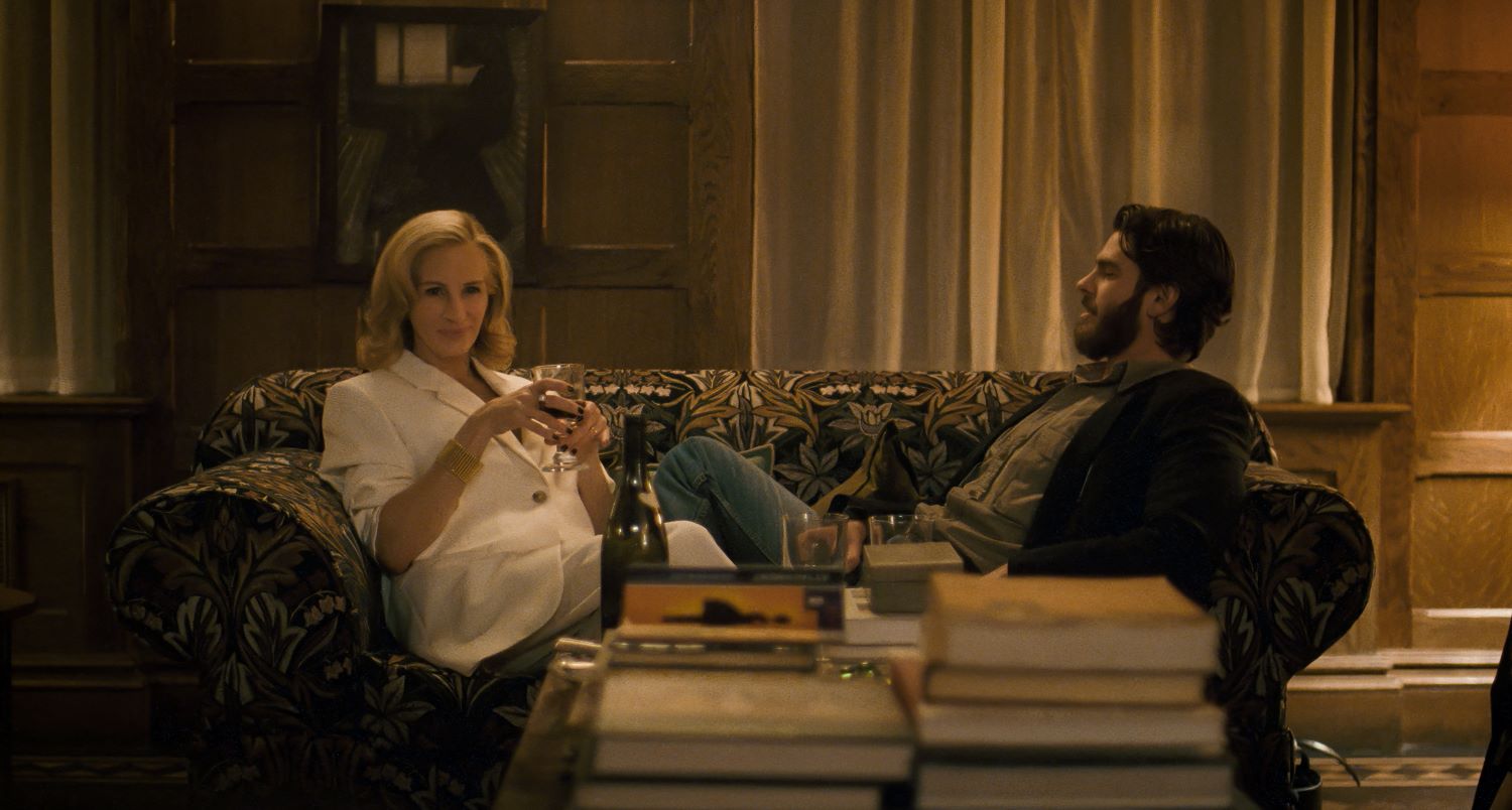 Un uomo e una donna seduti sul divano in salotto, davanti loro una pila di libri, una bottiglia di bino e un bicchere