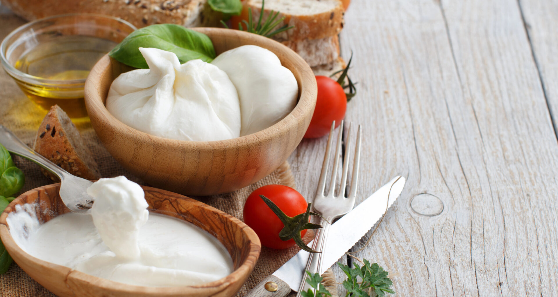 Una ciotola di burrata e una di stracciatella, accanto ad ingredienti della cucina italiana