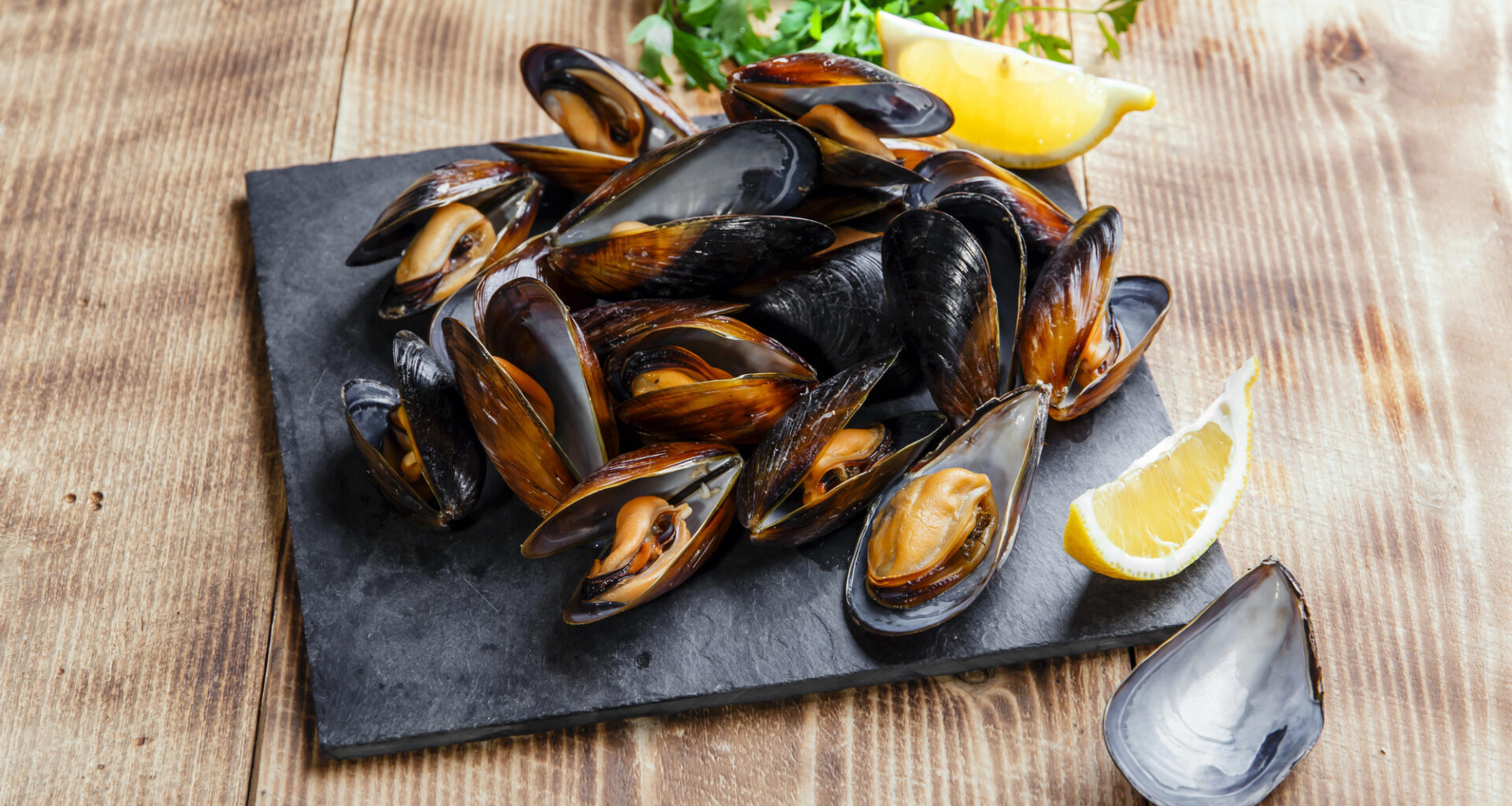 Cozze o mitili su vassoio di ardesia con limone e prezzemolo; concept: molluschi, frutti di mare
