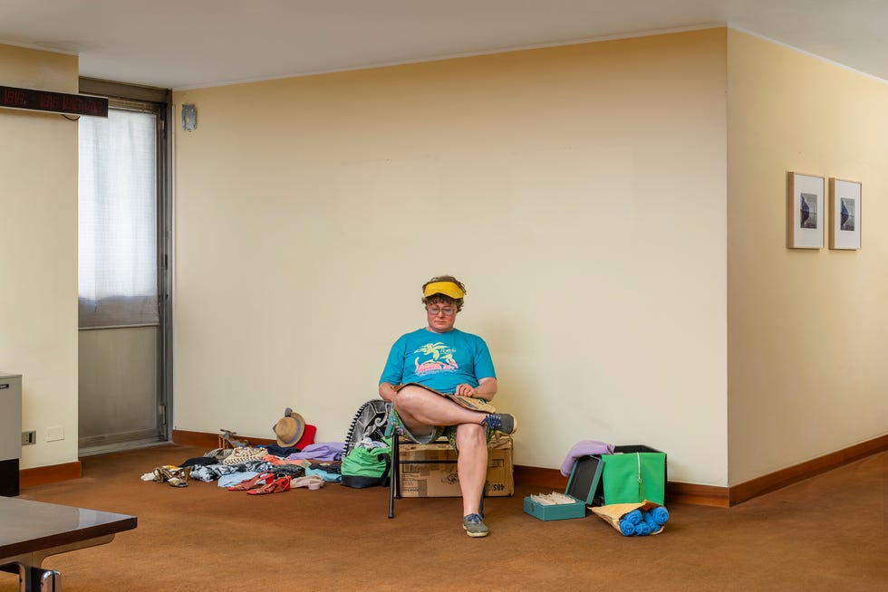 a person seated in a room with scattered clothing and objects around them