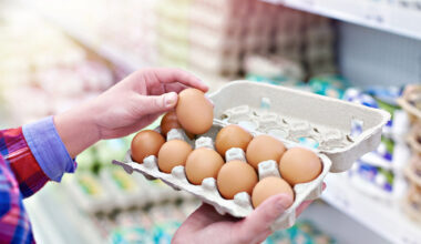 Una persona prende un uovo da un cartone da 12 uova nelle corsie di un supermercato