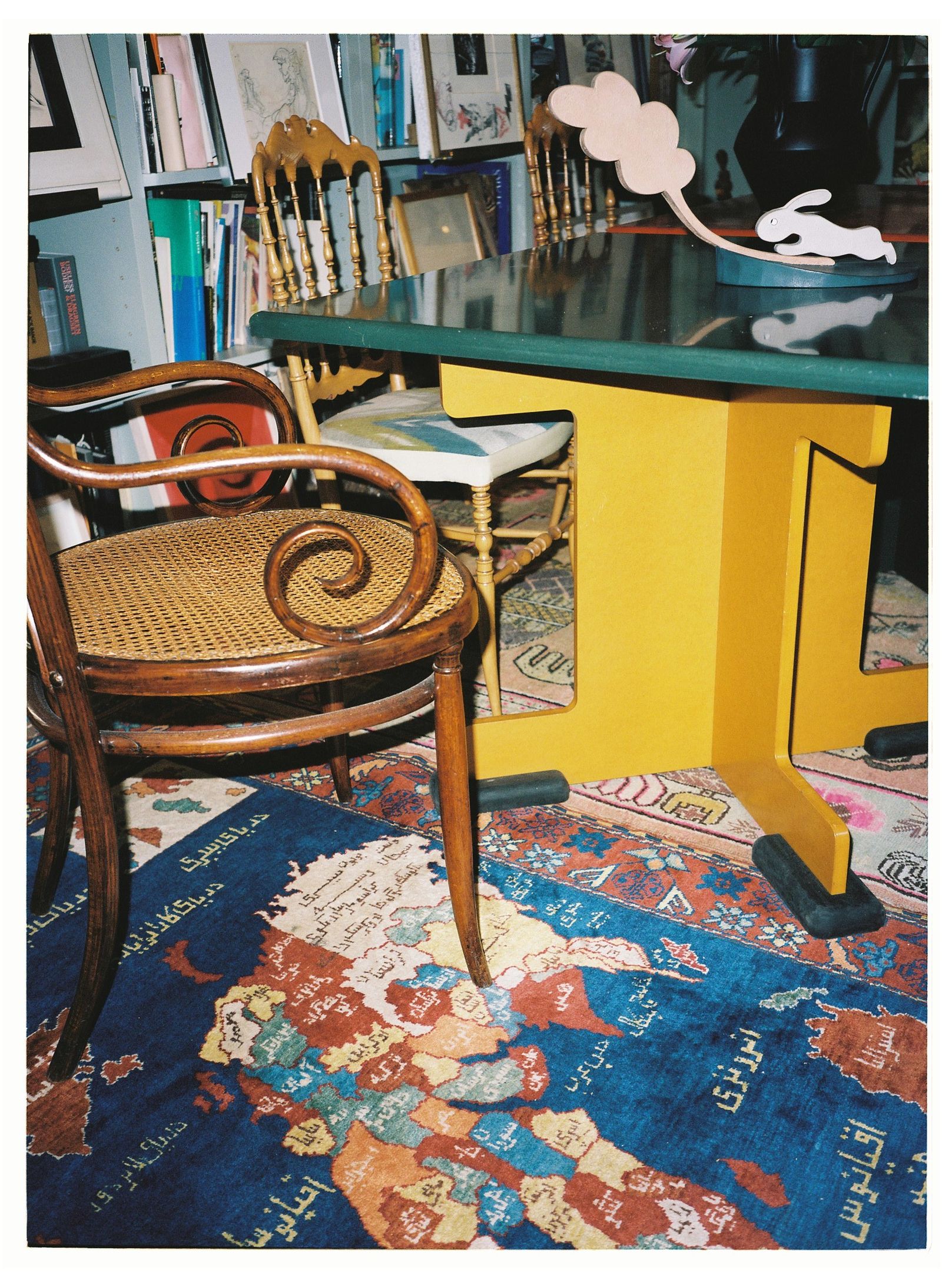 Soggiorno tavolo colorato con piano verde e base gialla sedie tappeto libreria libri