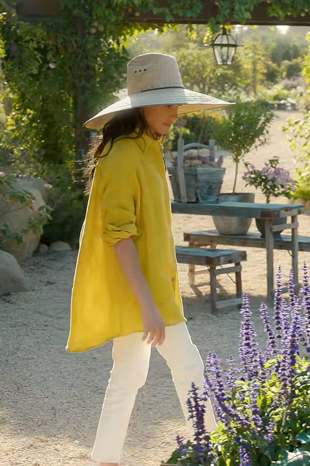 A woman walks in a garden filled with flowers and plants.