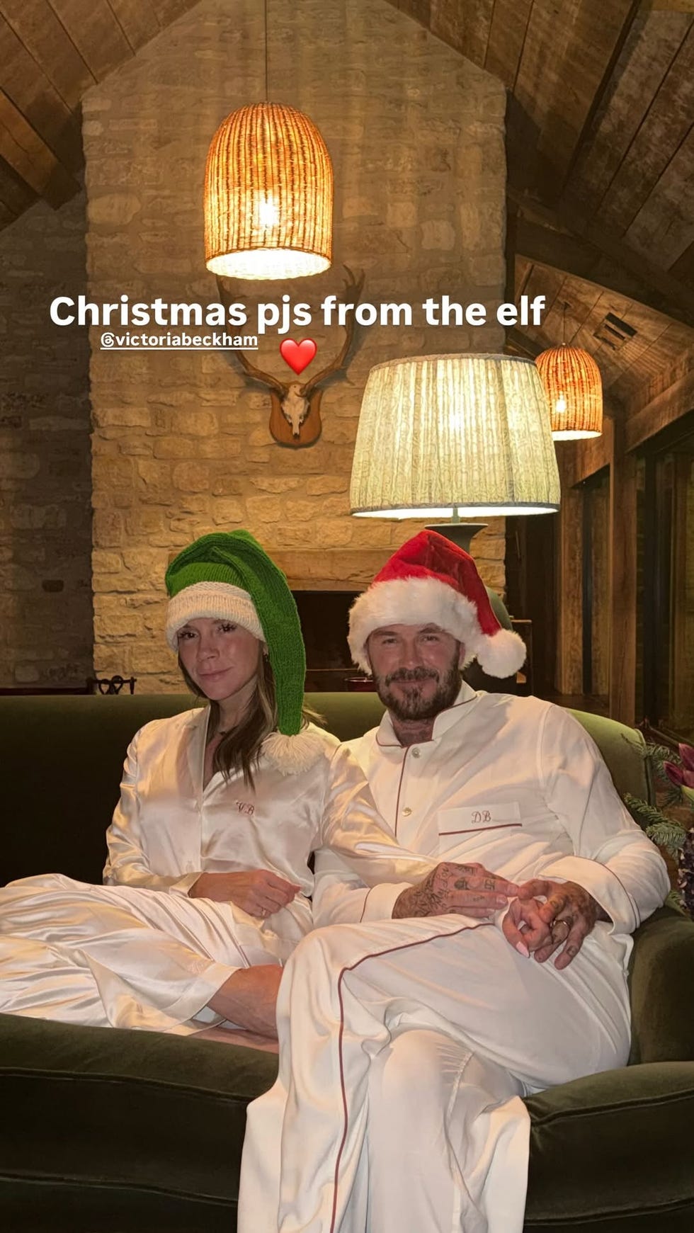 cozy holiday setting with two people wearing festive pajamas and hats seated on a couch