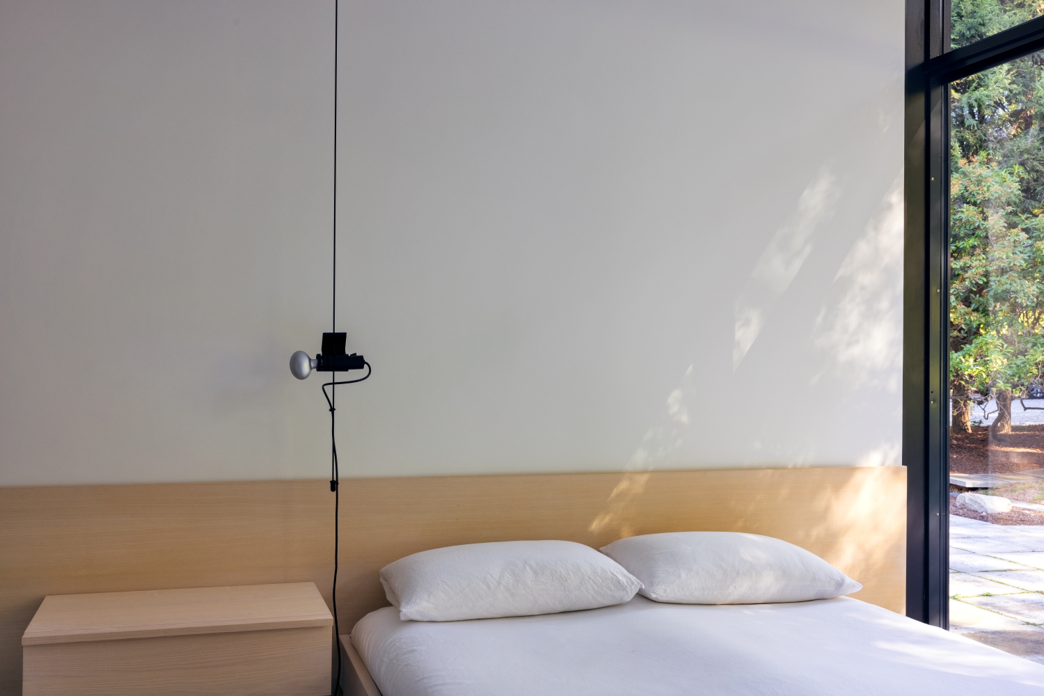 Camera da letto con lenzuola bianche, testiera e comodino di legno e lampada nera a sospensione