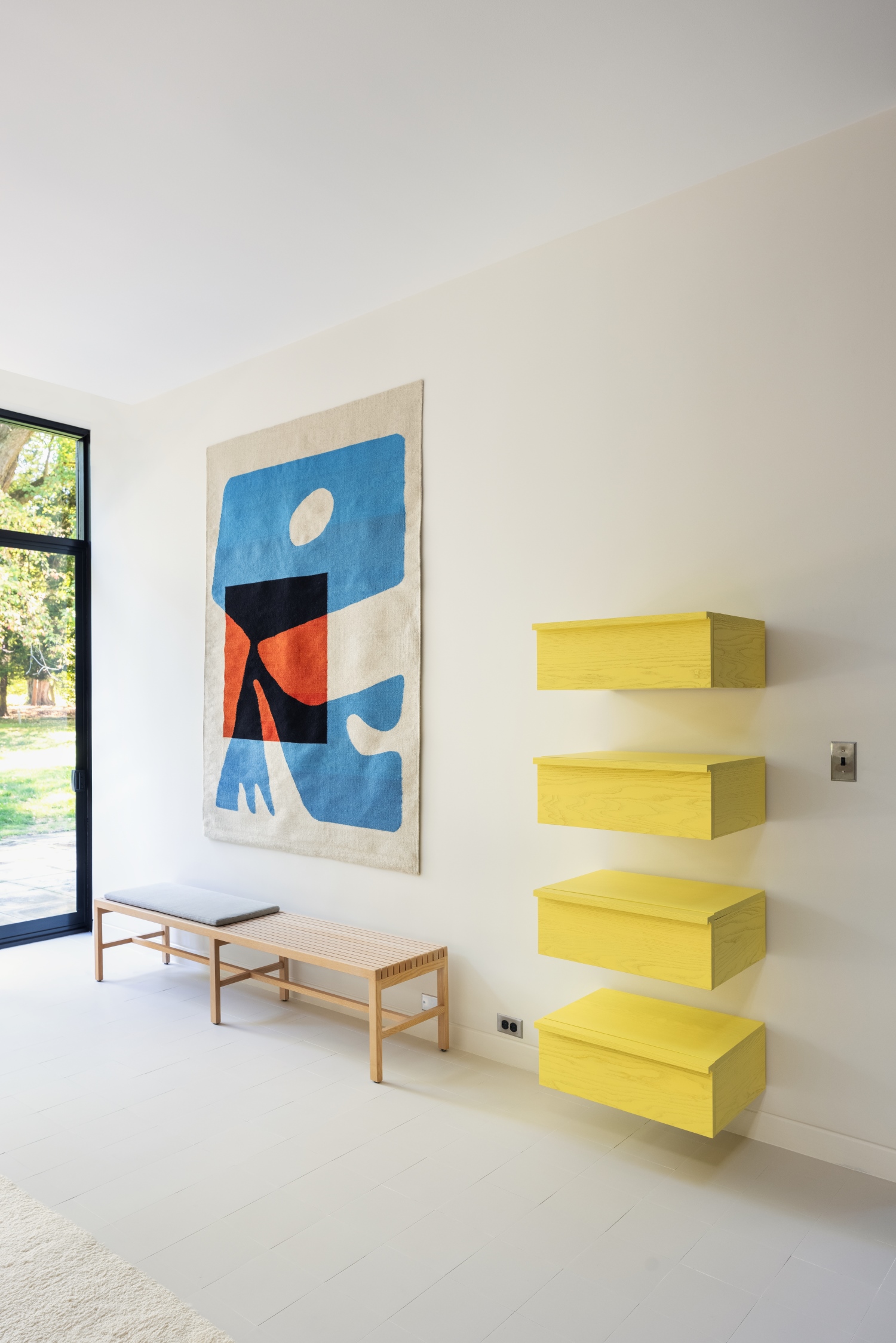 Piccole panche in legno, cassetti a muro gialli, quadro colorato e vetrata