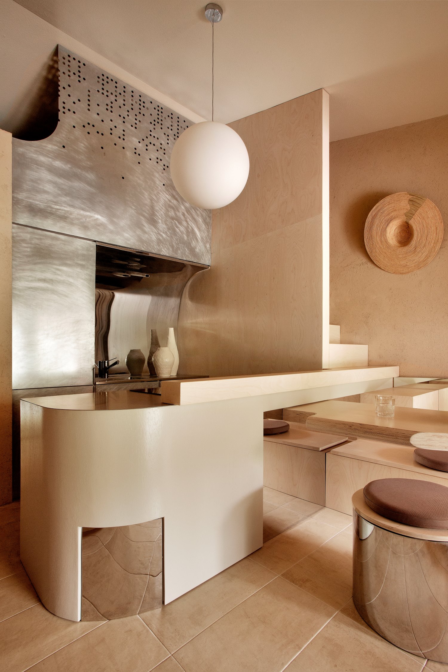 cucina sui toni del beige, lampadario rotondo bianco, pensili in acciaio e tavolo a sbalzo