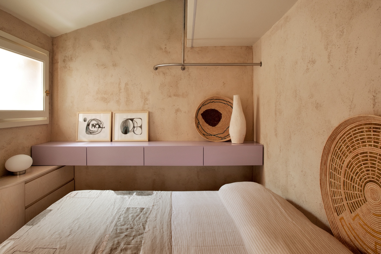 camera da letto con pareti bige, lenzuola bianche, mobili lilla e beige, quadri e vasi bianchi