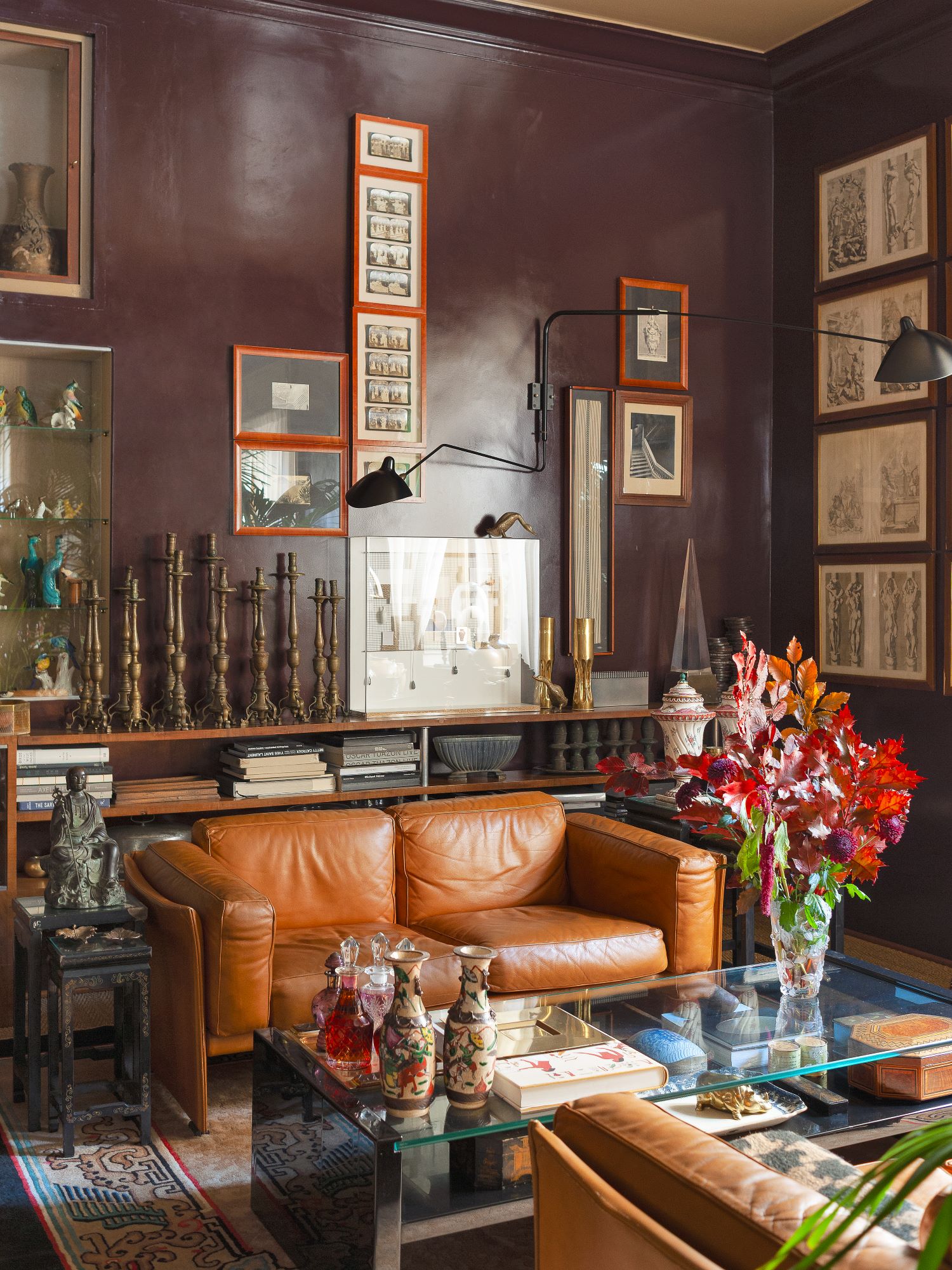 Zona living con divano in pelle marroncino, pareti marroni con quadri appesi, tavolino in vetro con vasi colorati appesi sopra