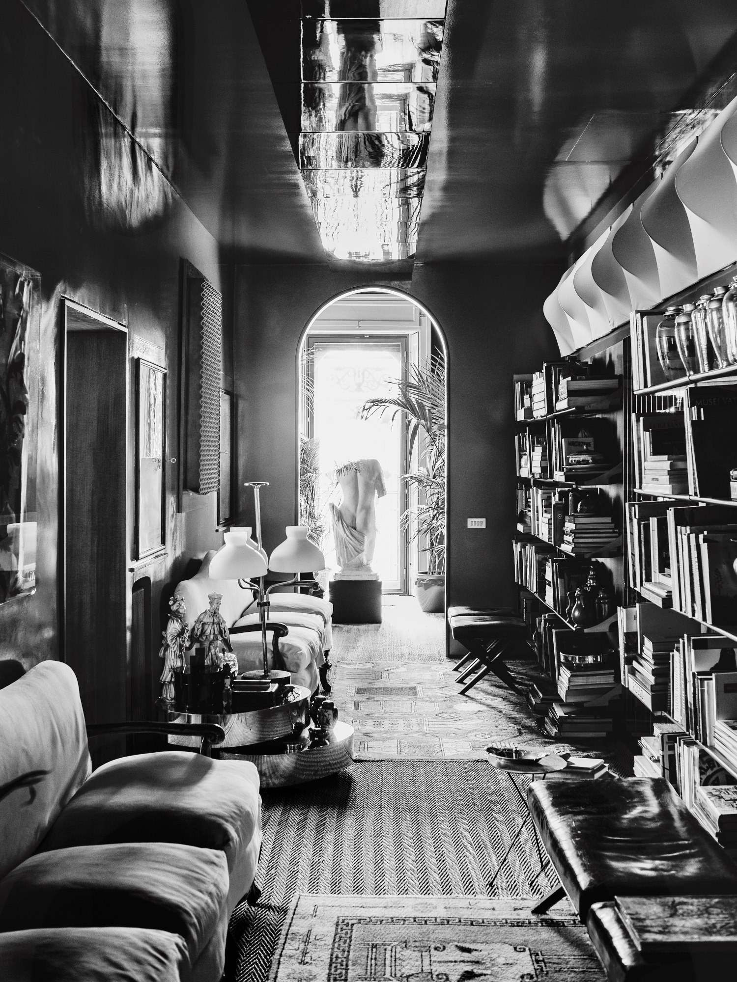 Corridoio con divani, lampade da tavolo, tappeti, librerie e pareti lucide