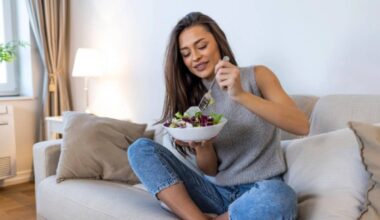 donna seduta sul divano che mangia un piatto di insalata