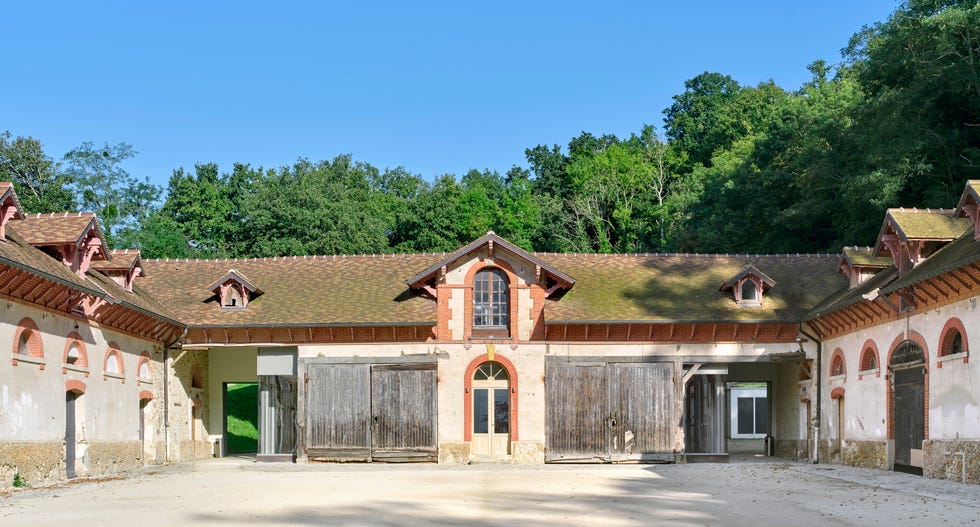 old building with wooden doors and an archway set against a forest backdrop and clear sky
