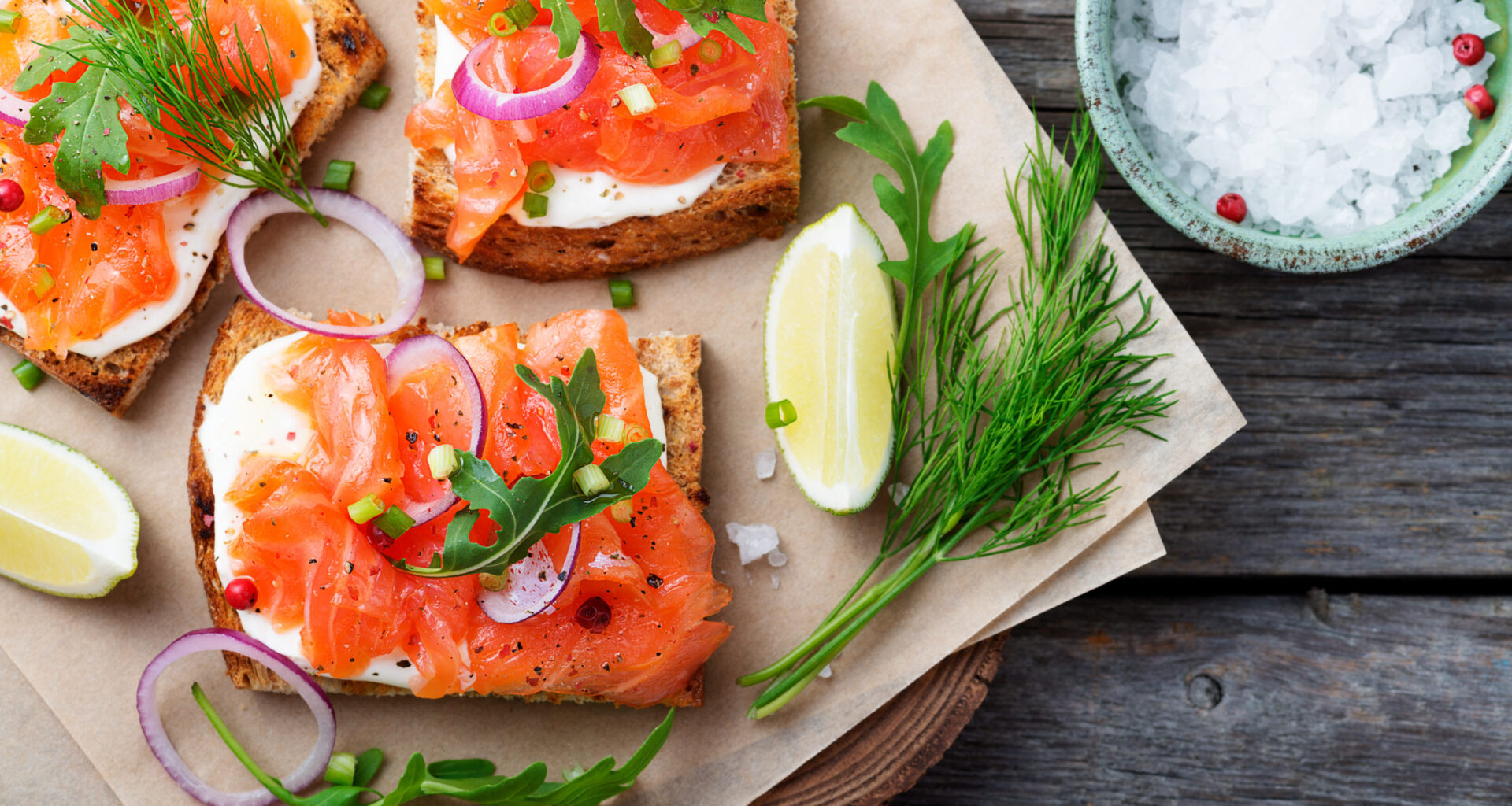 tartina salmone affumicato su tagliere con erbe aromatiche, lime e cipolla e ciotola di sale grosso