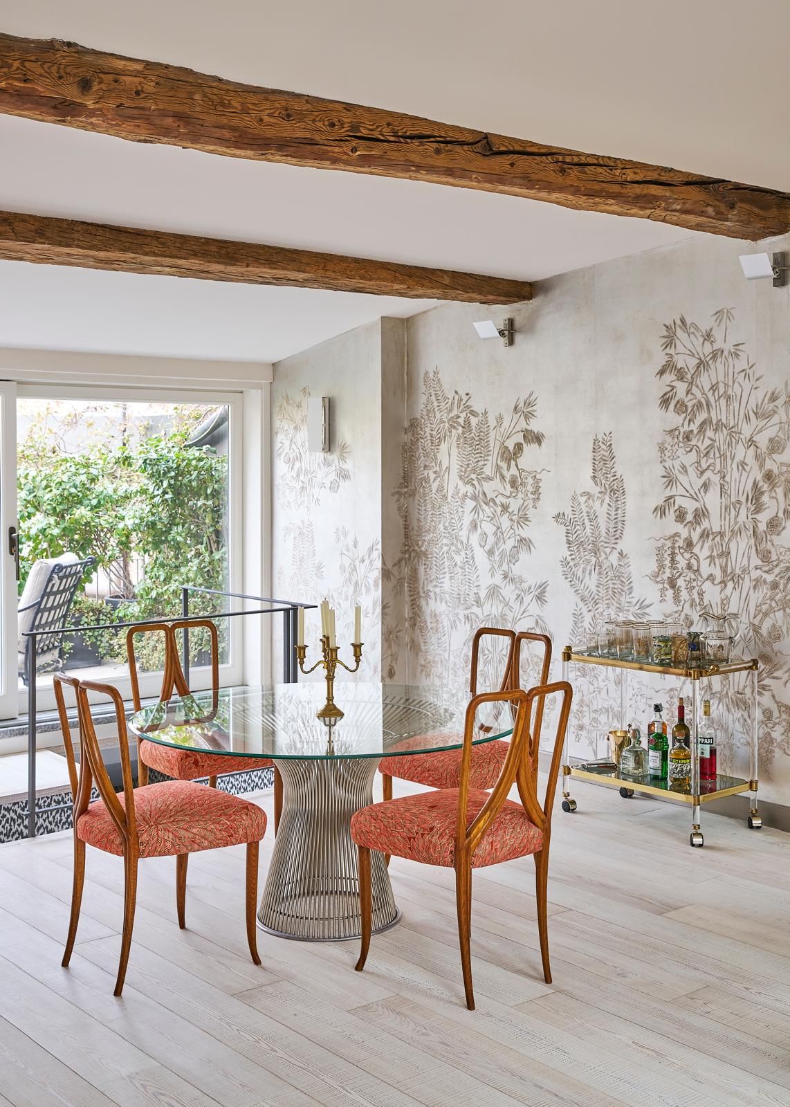 Tavolo in vetro sedie in legno e cusicini rossi parquet parete con decoro.