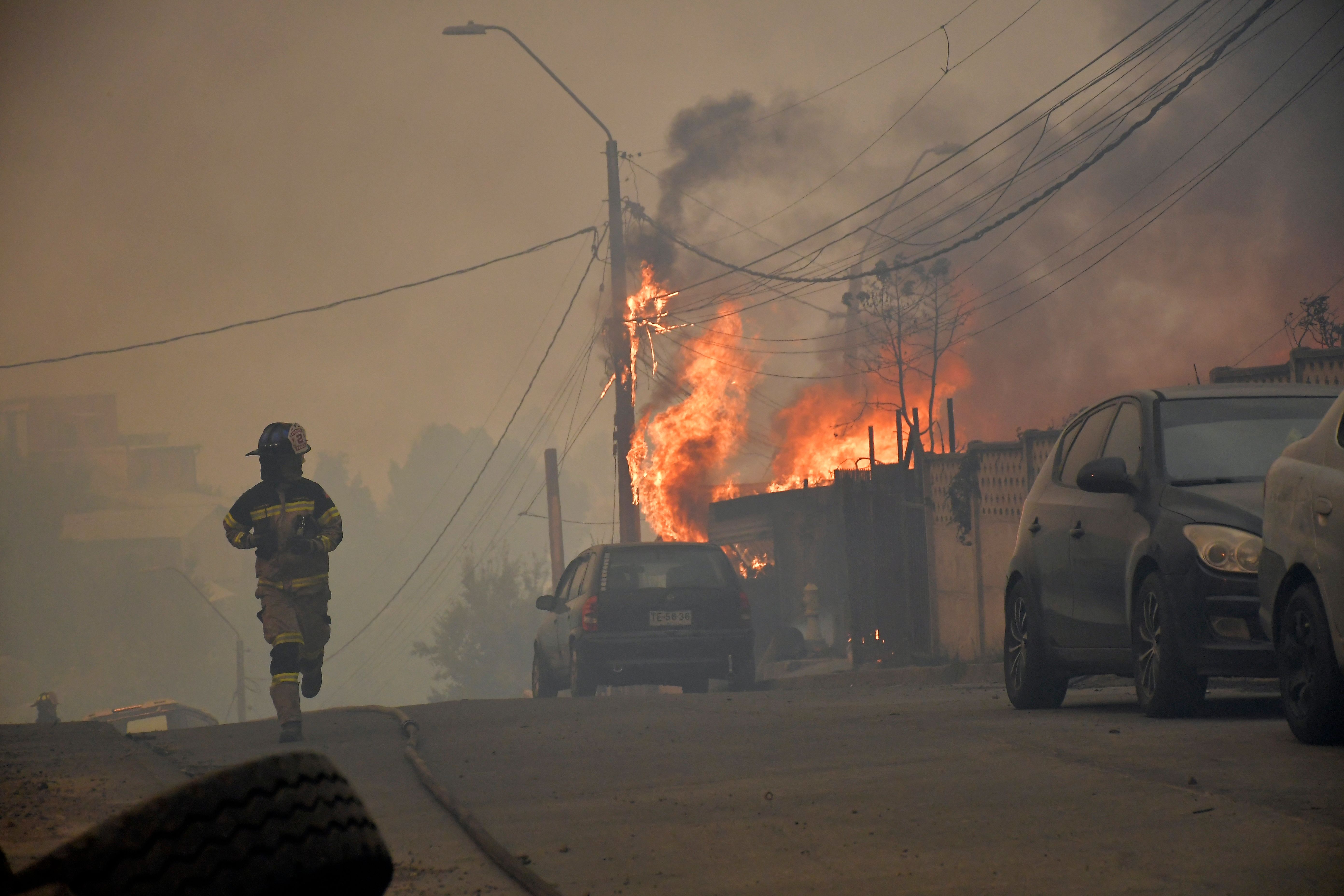TOPSHOT - A firefighter runs along a street as a house burns during a wildfire in Concepcion, Chile, on January 18, 2026. Chilean President Gabriel Boric declared a state of emergency on January 18 for two southern regions where raging wildfires h...