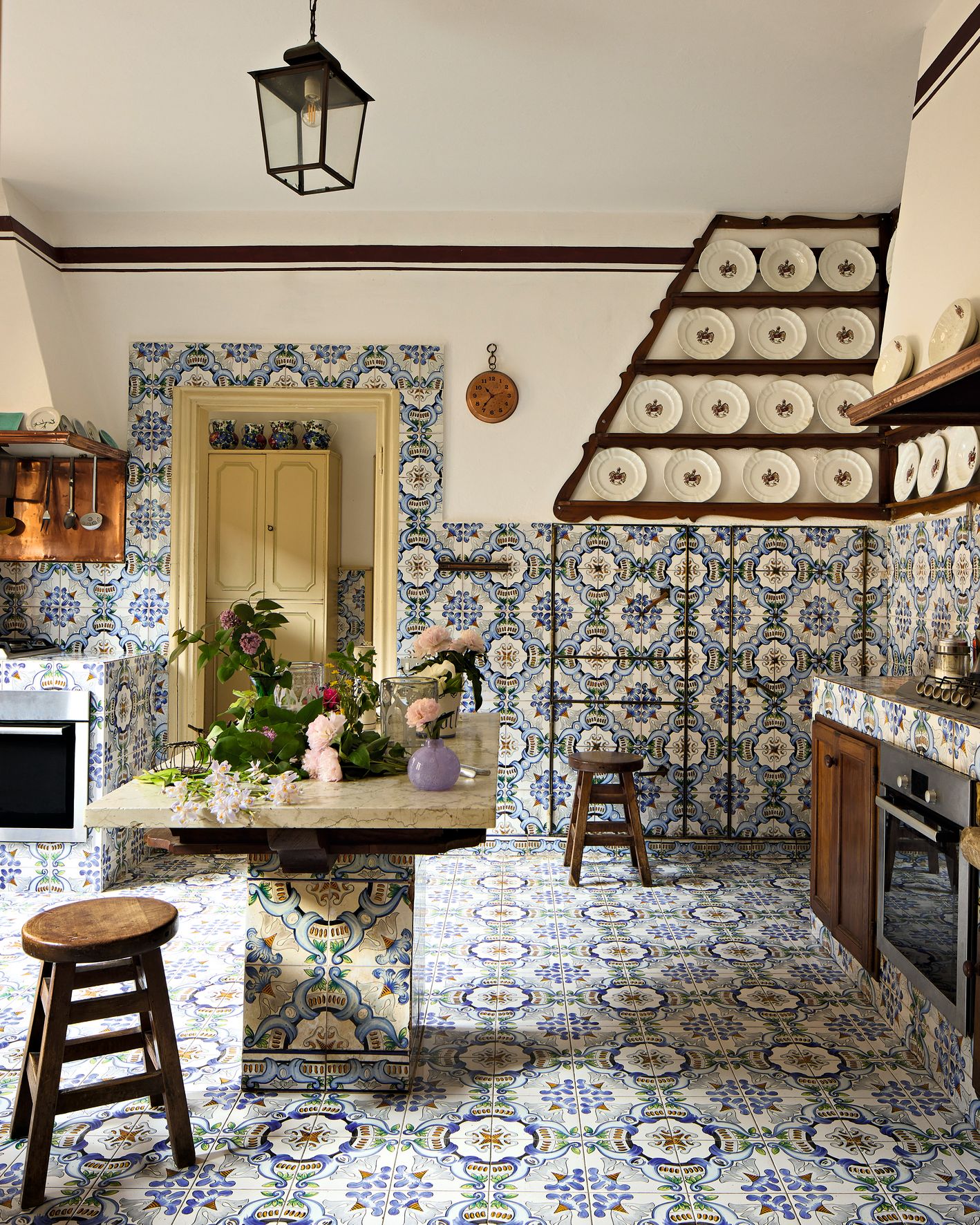 Cucina pavimento e pareti con piastrelle colorate blu bianche e gialle tavolo piatti alla parete forno utensili fiori
