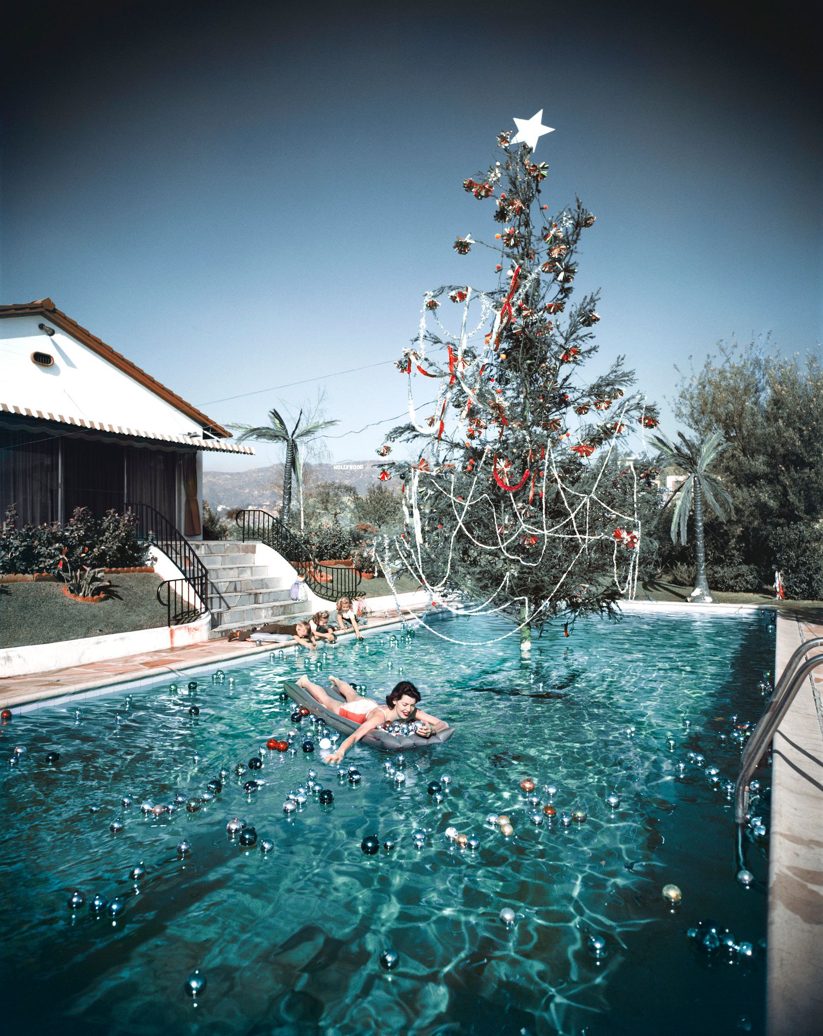 Rita Aarons moglie del fotografo Slim Aarons mentre nuota in una piscina decorata con palline galleggianti e un albero...