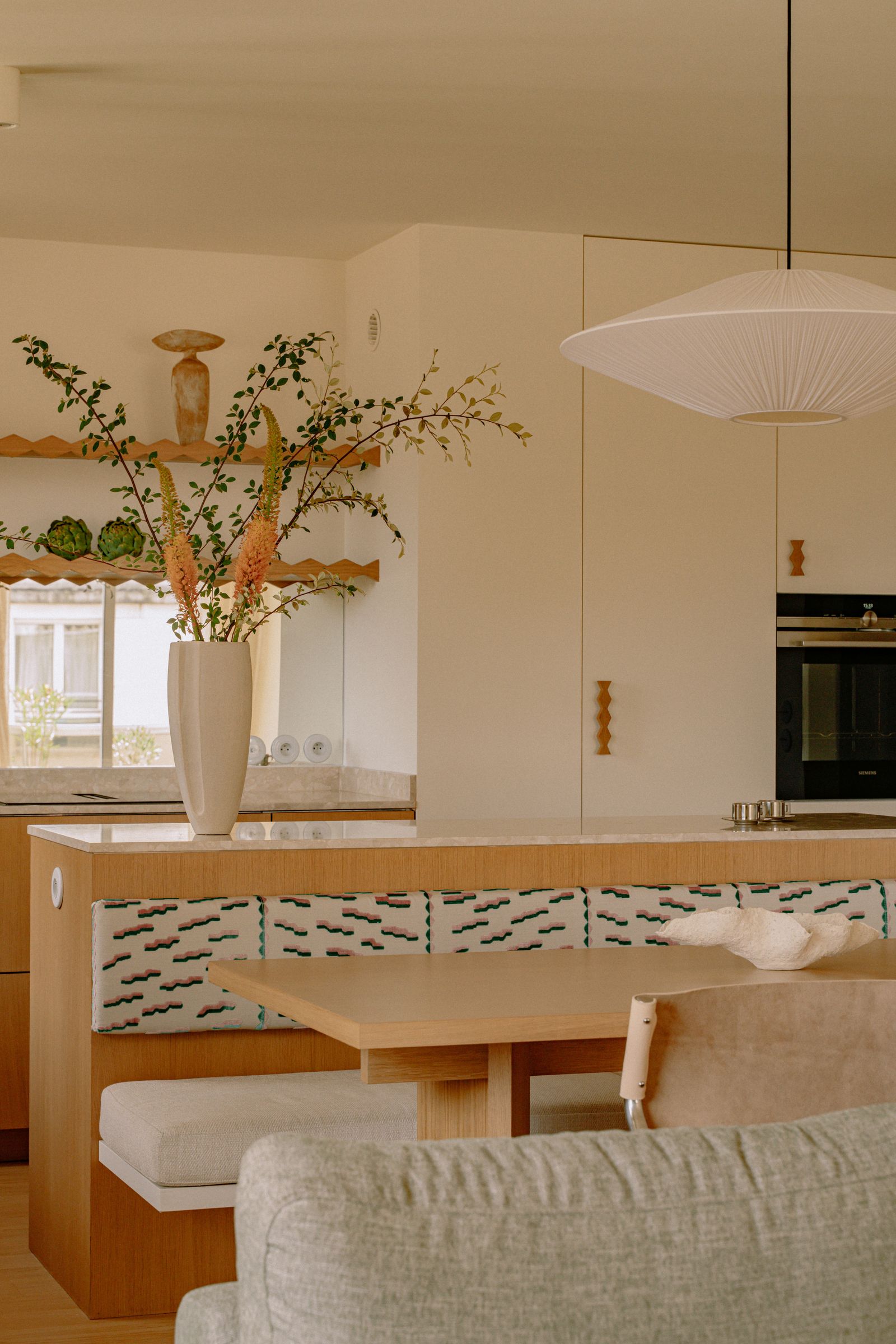 piccolo spazio cucina in legno chiaro con isola e panca vaso con fiori lampada