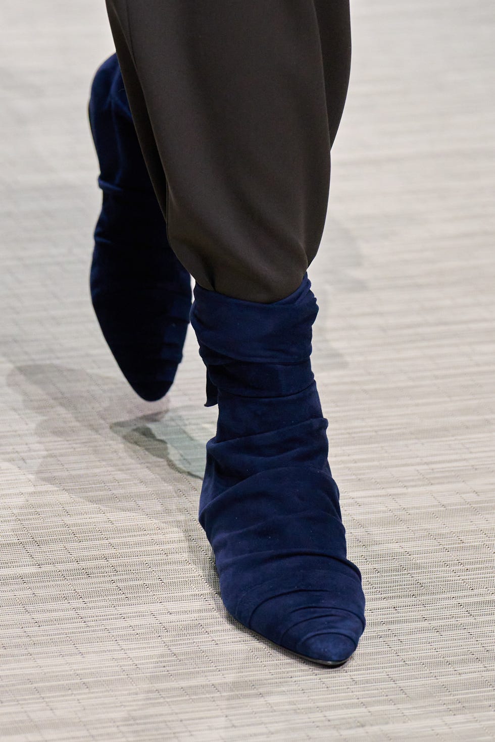 closeup of a leg wearing a stylish blue slouch boot on a textured surface