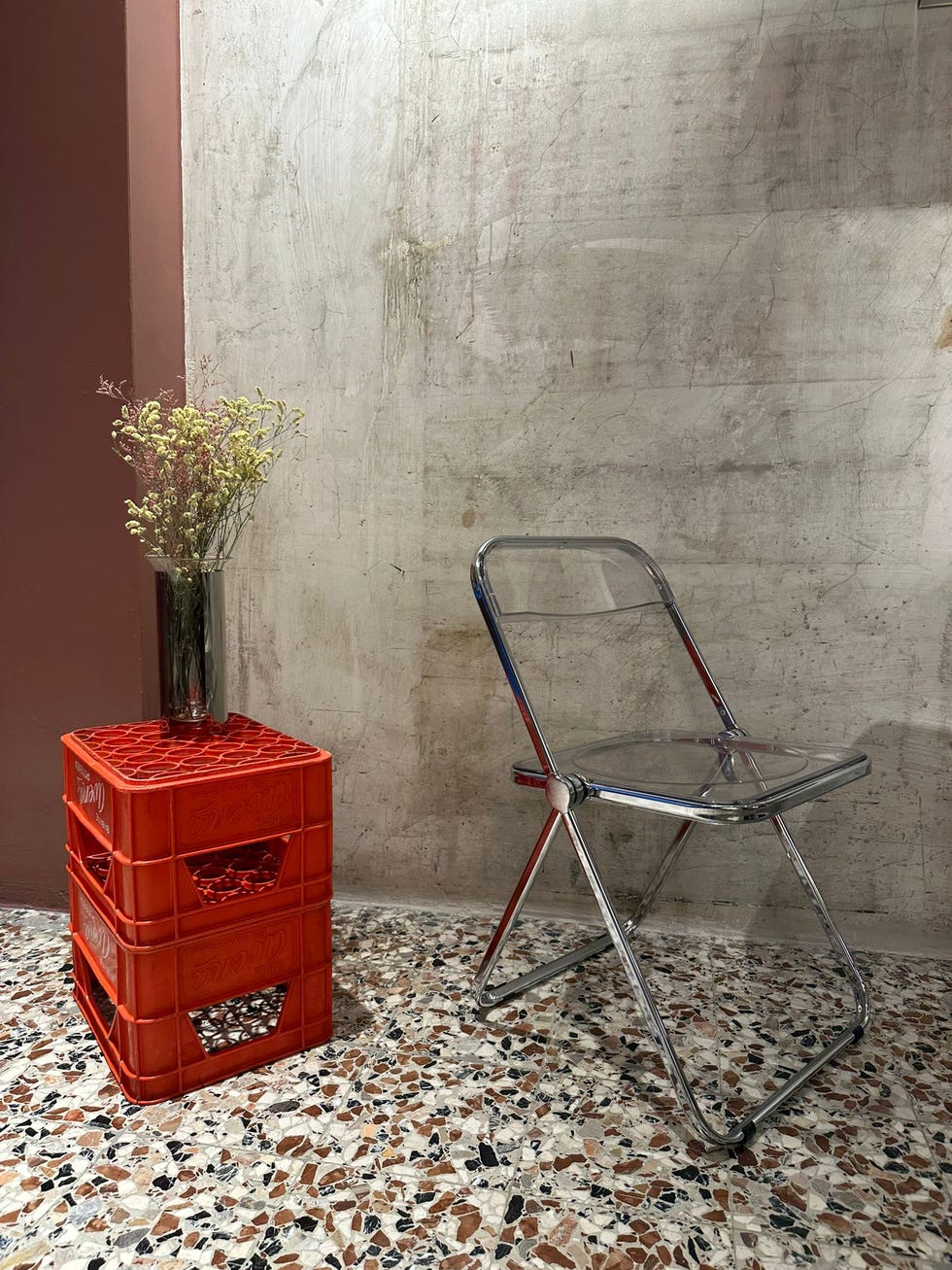 a transparent folding chair next to a red crate table with flowers