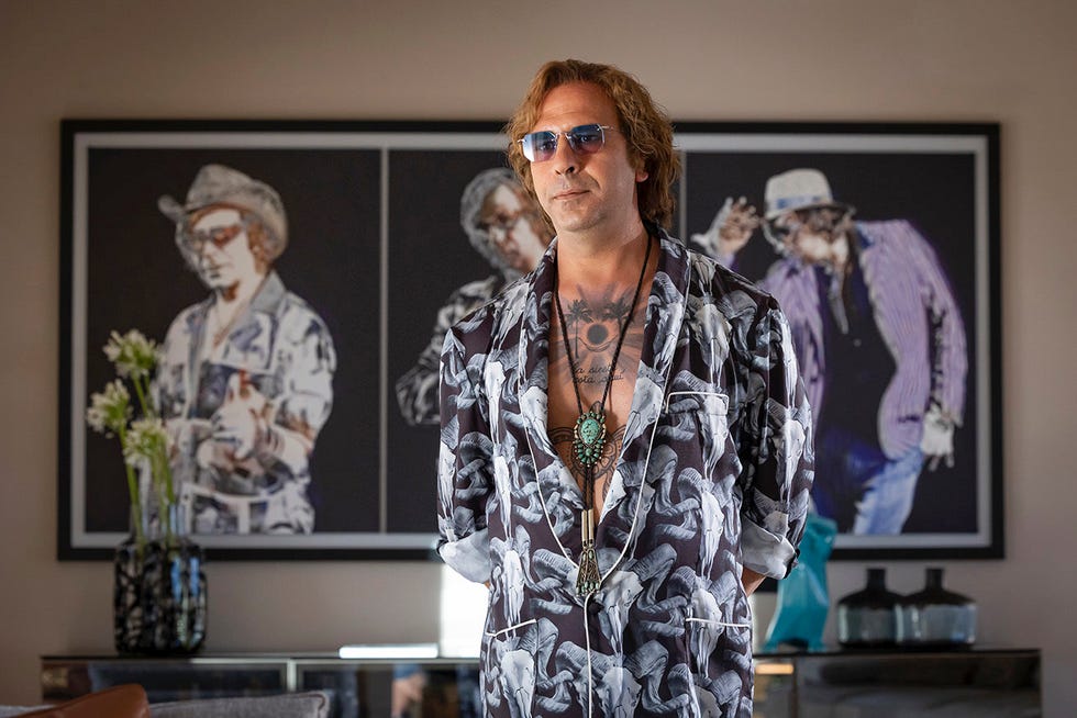 man with styled hair in a patterned shirt standing in front of artwork