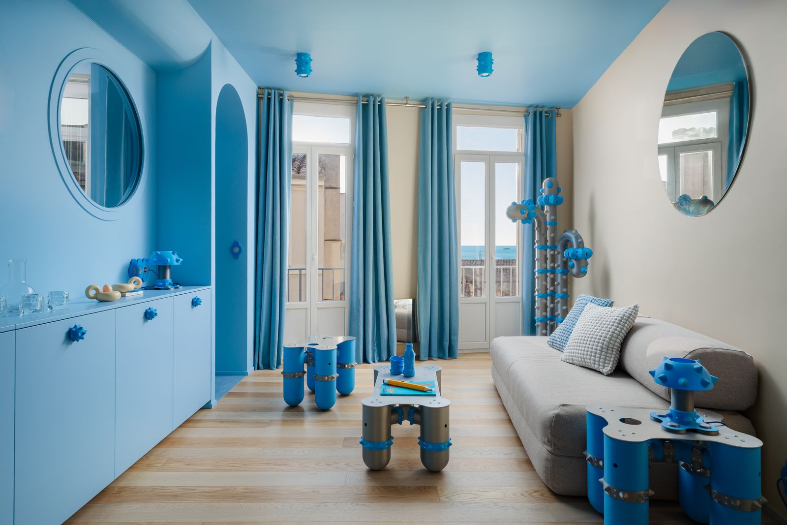 consolle lunga azzurra con oblò divano specchio rotondo tende tavolini