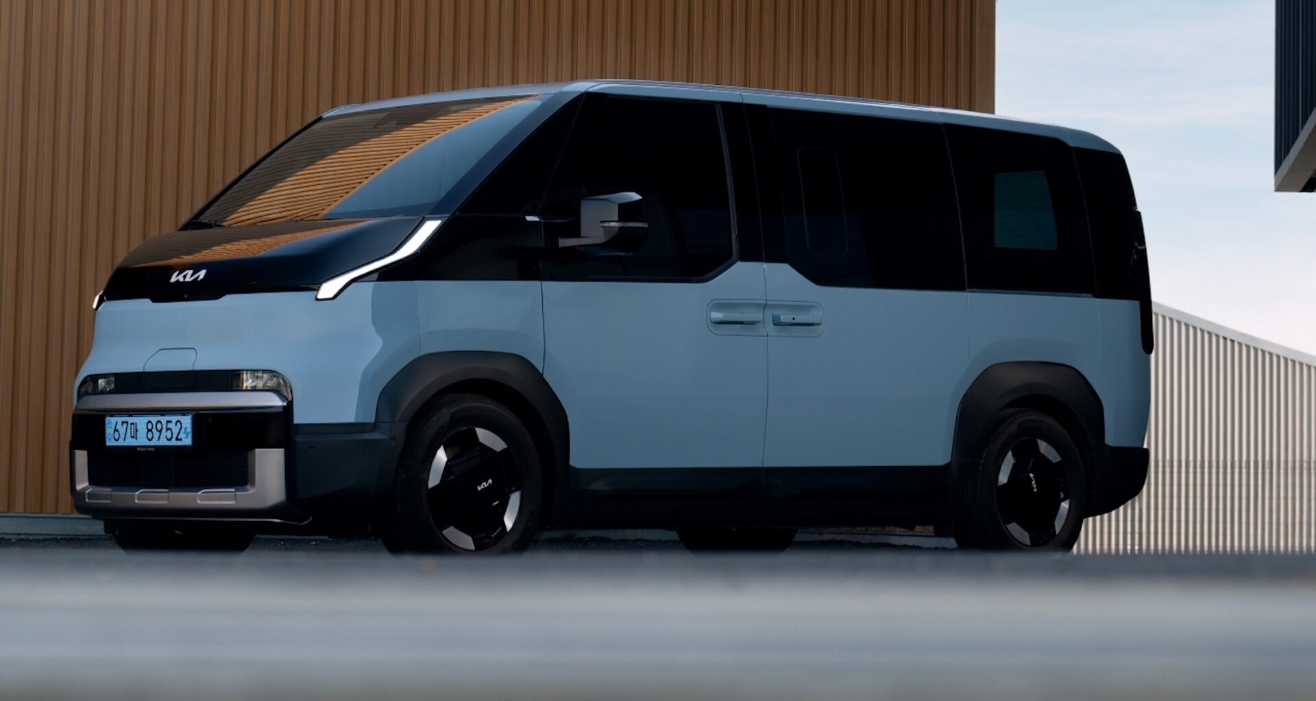 A modern, two-tone Kia electric van parked near a building with a textured brown wall.