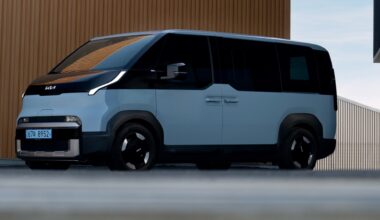 A modern, two-tone Kia electric van parked near a building with a textured brown wall.