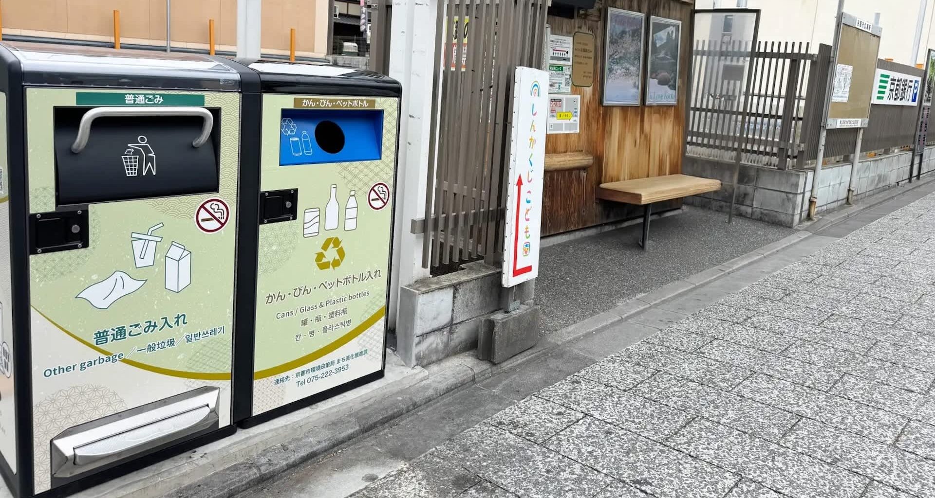 Two bins for waste disposal beside a wooden bench at a bus stop.