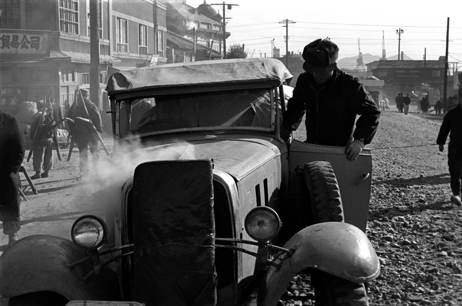 A man examines a car from which smoke is billowing.
