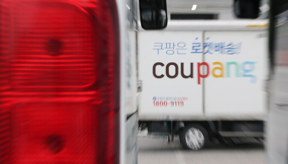 Delivery trucks and a Coupang logo at a logistics center in Seoul.