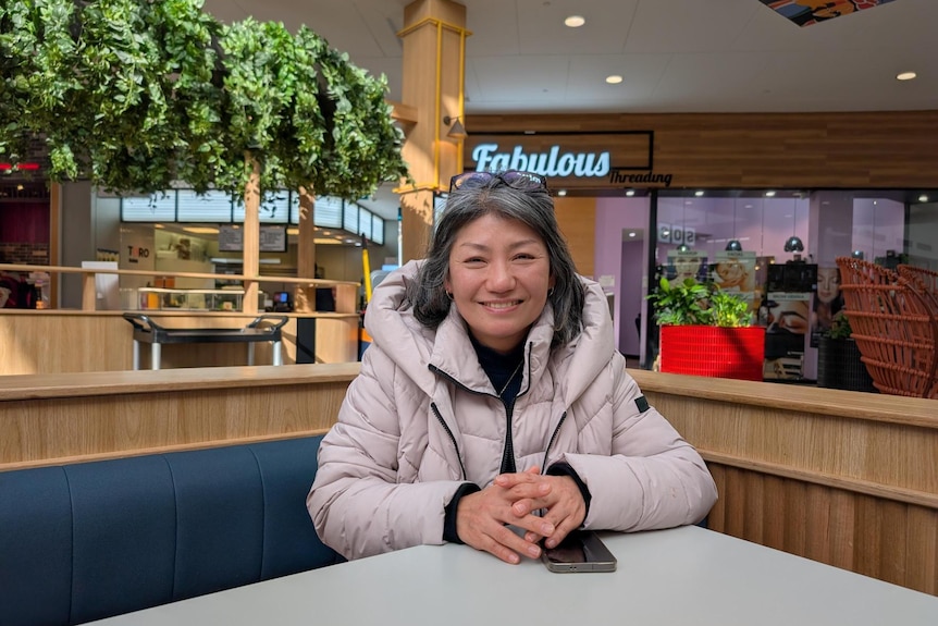A woman sits at a table smiling at a food court.
