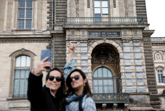 Tūristes pie izsistā loga, pa kuru laupītāji iekļuva Luvras muzejā.