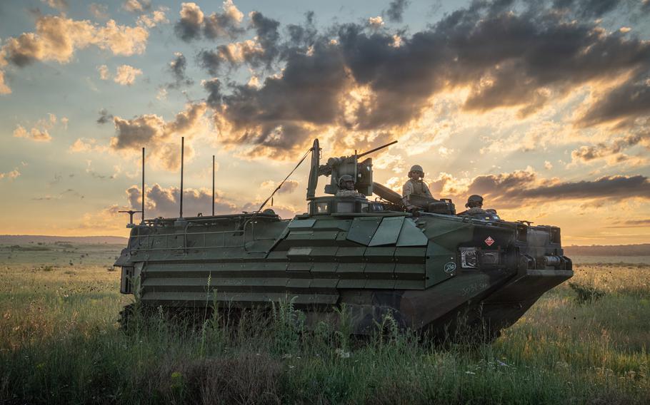 A military assault vehicle is parked in front of a beautiful orange sunrise.