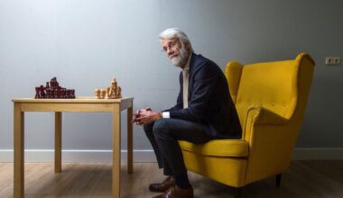 Man op een gele stoel achter een tafel met een schaakbord.