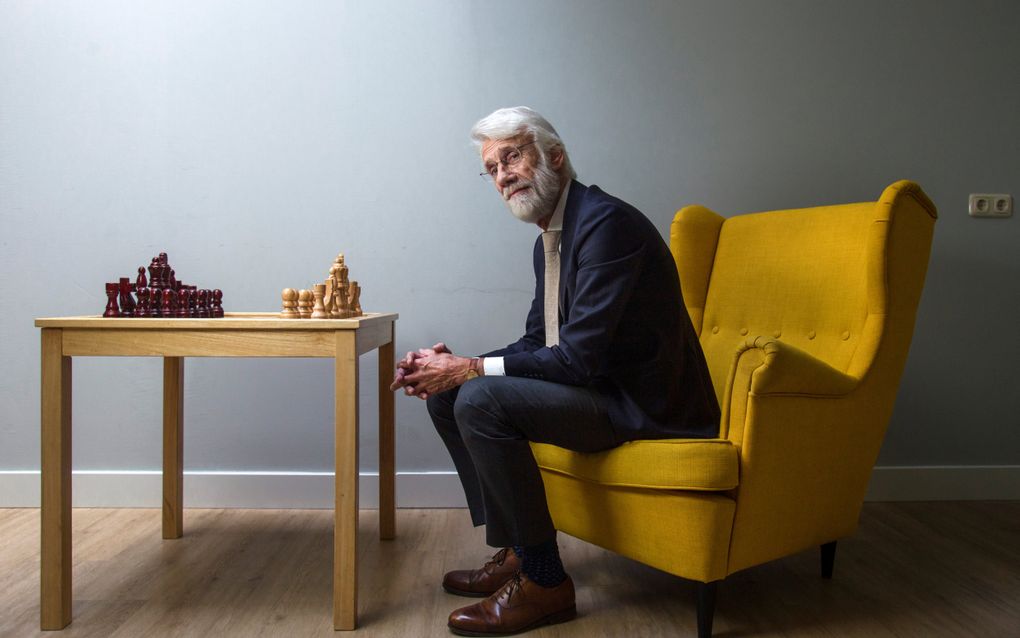 Man op een gele stoel achter een tafel met een schaakbord.