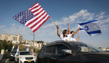 Twee vrouwen in wit T-shirt zwaaien met vlaggen vanuit een auto.