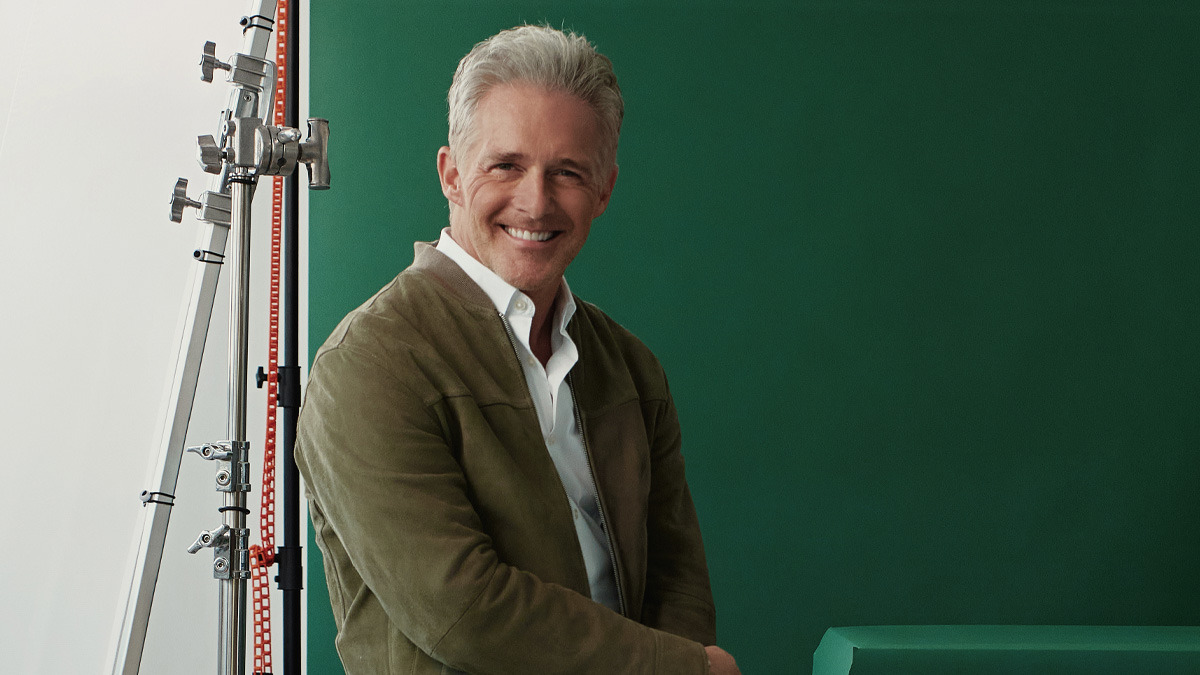 Christoff poseert in een leuk jasje en met een grote glimlach voor een groen scherm.