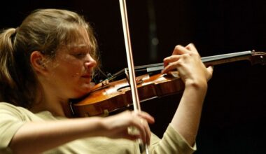 Een vrouw strijkt met een strijkstok over de snaren van de viool die ze viool onder haar kin heeft. Met haar linkerhand houdt ze de viool vast.