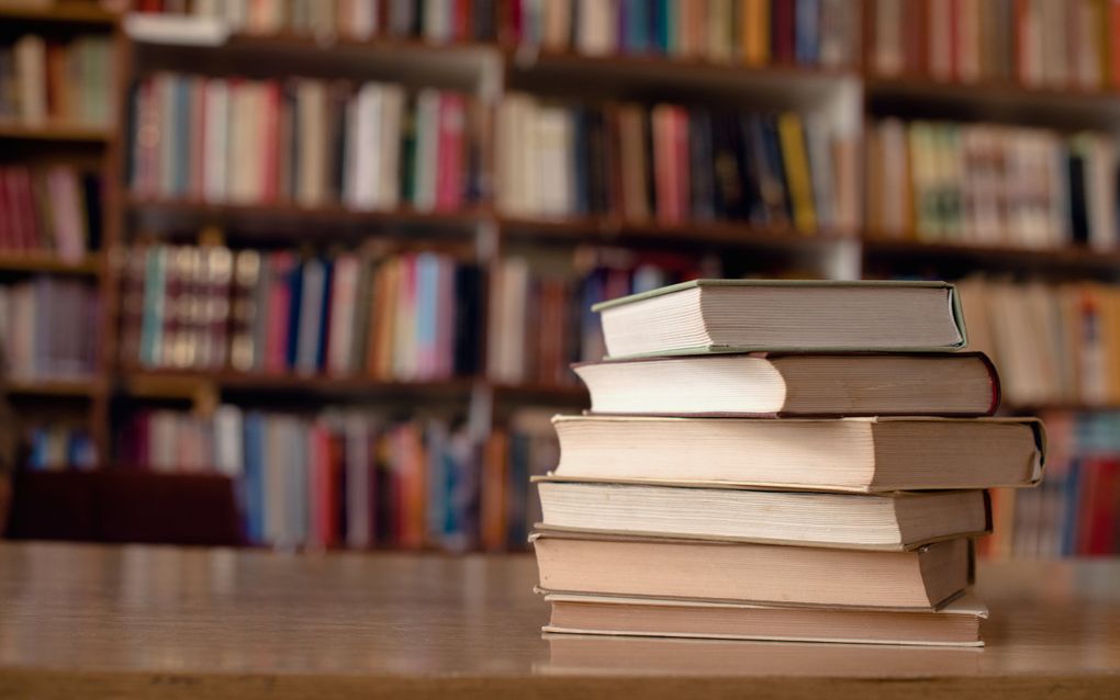 Een stapel boeken op een tafel, op de achtergrond boekenkasten.