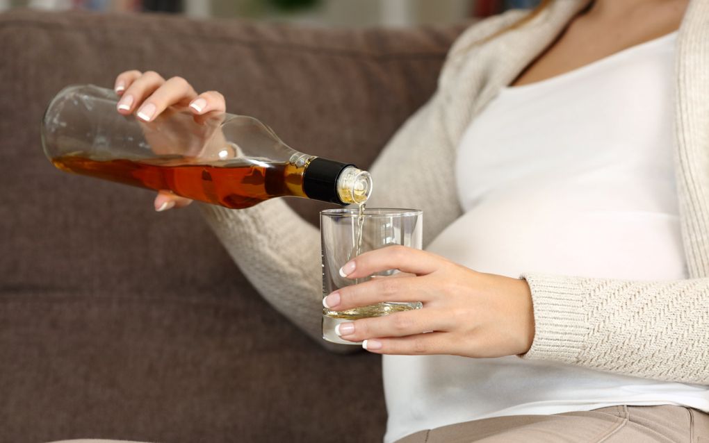 Een vrouw met een dikke buik schenkt wijn in een glas.