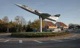 Een F-104 Starfighter staat op een rotonde, een herinnering aan de Belgische militaire luchtvaartgeschiedenis tijdens de Koude Oorlog.